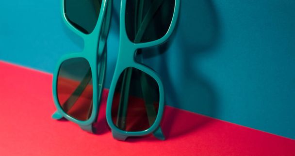 Sobre fondo rosa brillante se encuentran las gafas de sol en marco azul plástico con gafas oscuras. Verano. Accesorios
. - Foto, Imagen
