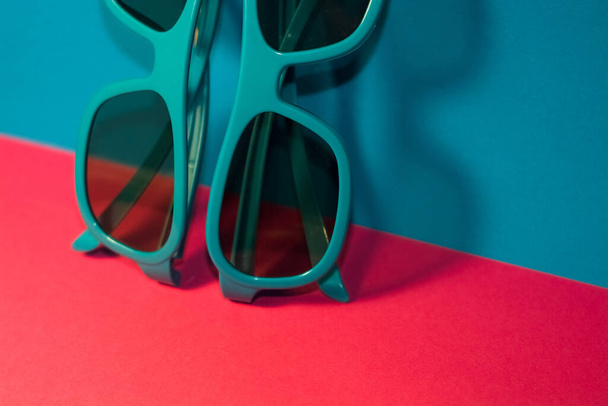 Sur fond rose vif reposent des lunettes de soleil dans un cadre en plastique bleu avec des lunettes sombres. L'été. Accessoires
. - Photo, image