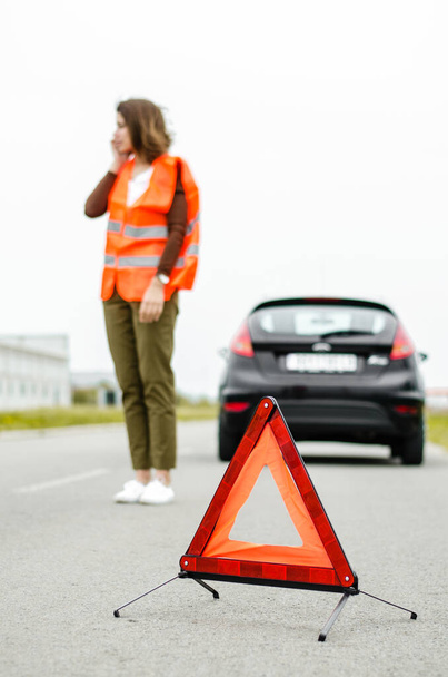 Красный треугольник на дороге, проблемы с машиной, одинокая девушка, объясняющая ситуацию по телефону
 - Фото, изображение