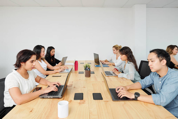 Молоді розробники програмного забезпечення, що працюють на ноутбуках за великим дерев'яним офісним столом
 - Фото, зображення