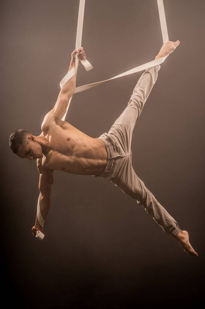 circus artist on the aerial straps with Strong muscles on the background of smoke - Foto, Imagem