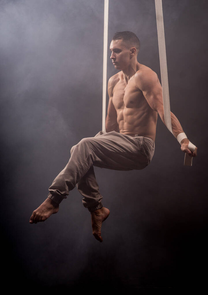 circus artist on the aerial straps with Strong muscles on the background of smoke - Foto, afbeelding