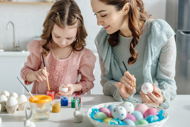 επιλεκτική εστίαση της ευτυχούς μητέρας και της κόρης ζωγραφική πασχαλινά αυγά κοντά διακοσμητικά κουνέλια  - Φωτογραφία, εικόνα