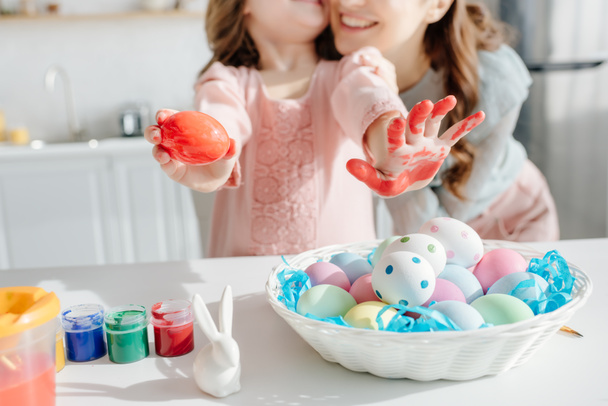 selective focus of painted easter eggs near decorative rabbit, mother and daughter  - Foto, Imagem