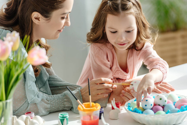 happy mother and cheerful child painting easter eggs near flowers - Foto, Imagem