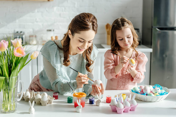 selective focus of cute child and mother painting easter eggs near tulips  - Foto, imagen