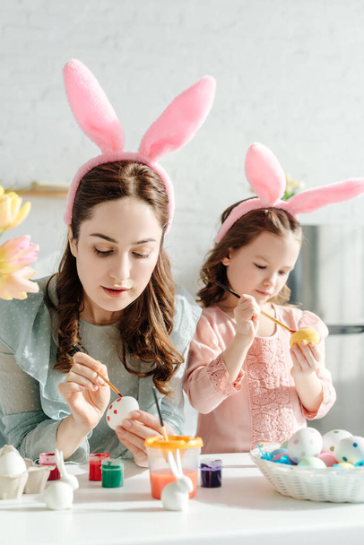 selective focus of mother and kid in bunny ears painting chicken eggs  - Photo, Image