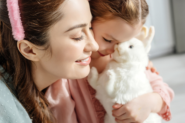 おもちゃのウサギとかわいい子供の近くの幸せな母親の選択的な焦点  - 写真・画像