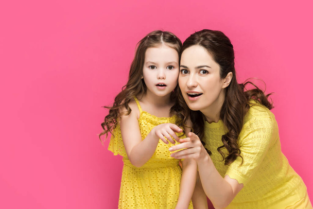 surprised mother and daughter pointing with fingers isolated on pink  - Foto, afbeelding