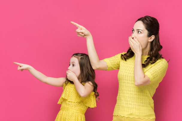 Schockierte Mutter und überraschtes Kind bedecken Mund isoliert auf rosa  - Foto, Bild