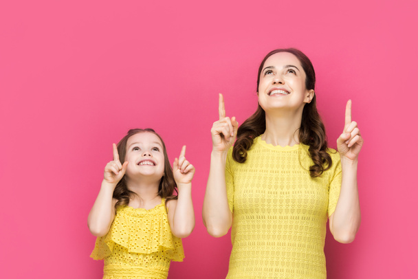 happy woman and kid pointing with fingers isolated on pink  - Photo, Image