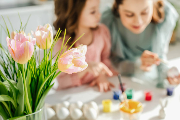 selective focus of tulips near mother and daughter painting easter eggs  - Φωτογραφία, εικόνα