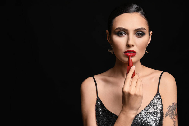 Beautiful young woman applying makeup against dark background - Foto, Imagen