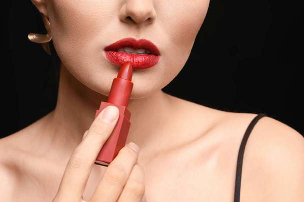 Beautiful young woman applying makeup against dark background, closeup - Foto, afbeelding