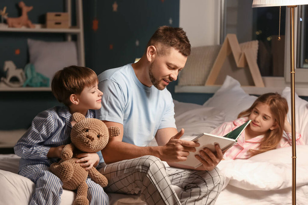 Vader en zijn kleine kinderen lezen thuis een verhaaltje voor het slapen gaan - Foto, afbeelding