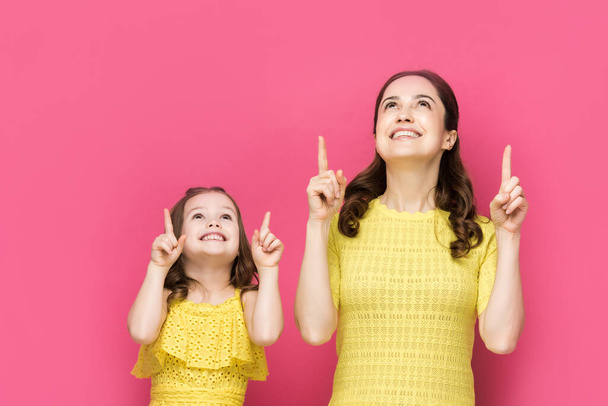 glückliche Mutter und Kind zeigen mit den Fingern und schauen vereinzelt auf rosa  - Foto, Bild