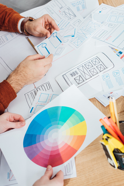 Καλλιεργημένη άποψη των σχεδιαστών που εργάζονται με τα πρότυπα του σχεδιασμού ux και του κύκλου χρώματος στο τραπέζι - Φωτογραφία, εικόνα