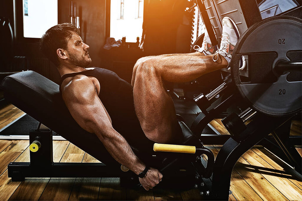 Homem atlético treina pernas no simulador no ginásio com peso. Corpo atlético, estilo de vida saudável, motivação fitness, corpo positivo
. - Foto, Imagem