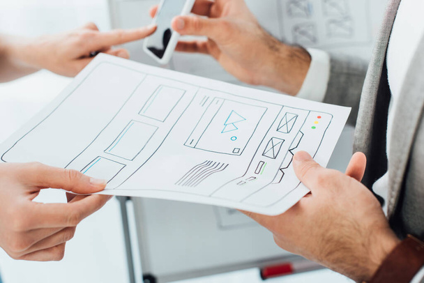 Cropped view of ux developers using smartphone and template of website near whiteboard isolated on white - Φωτογραφία, εικόνα