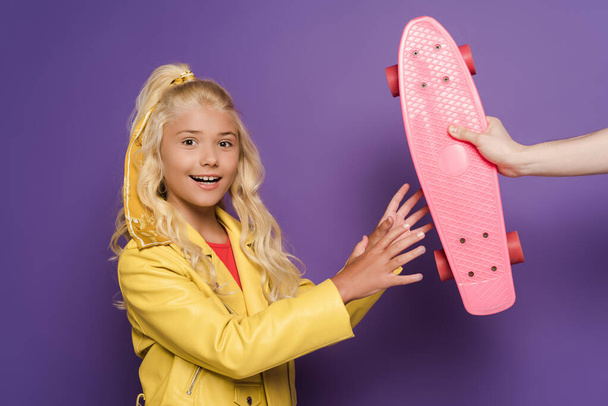 cropped view of man giving penny board to smiling kid on purple background  - Zdjęcie, obraz