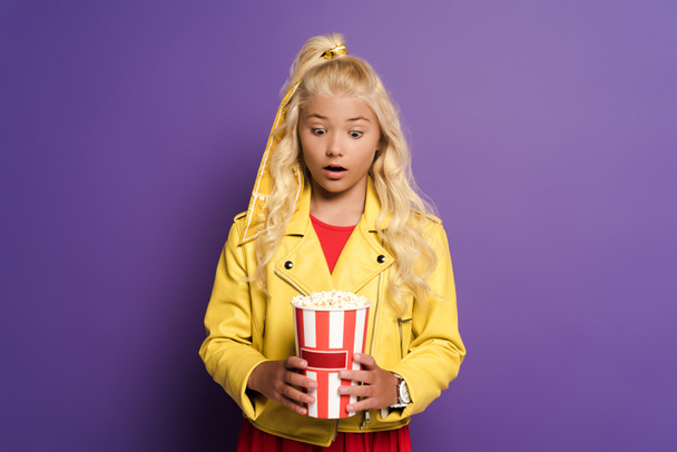 bambino scioccato che tiene secchio con popcorn su sfondo viola
  - Foto, immagini