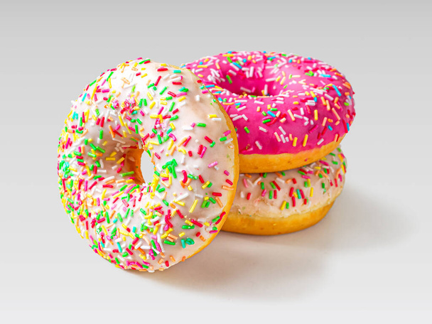 Três tradicionais donuts vitrificados americanos, dois de baunilha e um de cor de morango, encontram-se em um fundo claro.
 - Foto, Imagem