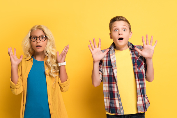 shocked kids with outstretched hands looking at camera on yellow background  - Foto, Imagem