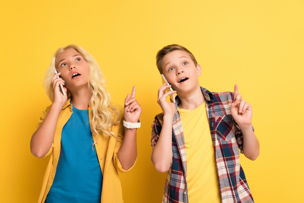 zasněné děti ukazující myšlenkové gesto a mluvení na chytrých telefonech na žlutém pozadí  - Fotografie, Obrázek