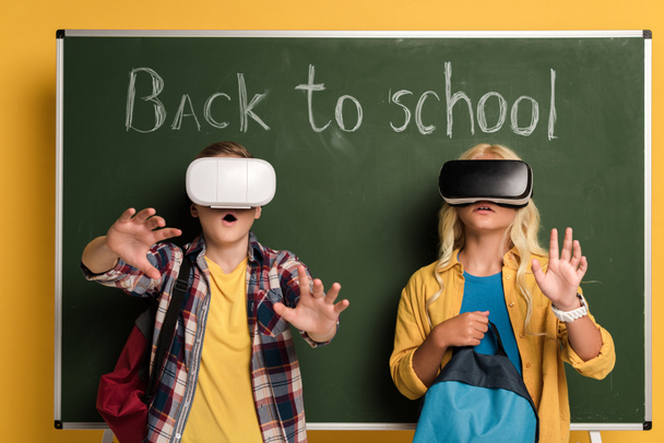 потрясенные школьники с гарнитурами виртуальной реальности, стоящими рядом с доской с надписью
 - Фото, изображение