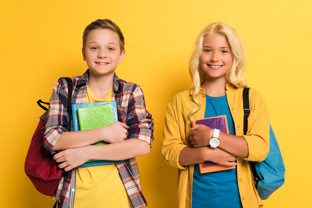 Lächelnde Schulkinder mit Büchern, die auf gelbem Hintergrund in die Kamera schauen  - Foto, Bild