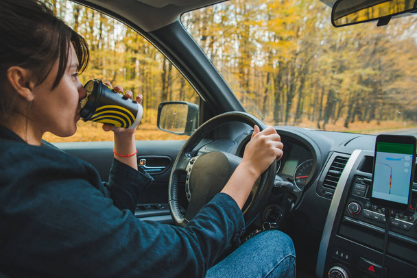 mujer conduciendo coche en otoño speedway beber café estilo de vida viaje por carretera
 - Foto, imagen