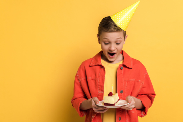 黄色の背景に誕生日ケーキ付きのショックを受けた子供は  - 写真・画像