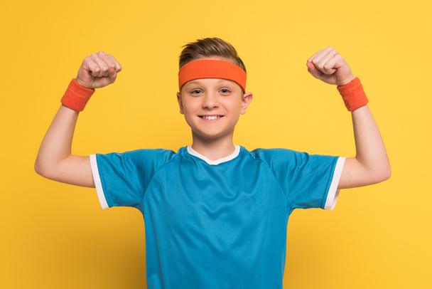 uśmiechnięty dzieciak w odzieży sportowej pokazujący silny gest na żółtym tle  - Zdjęcie, obraz