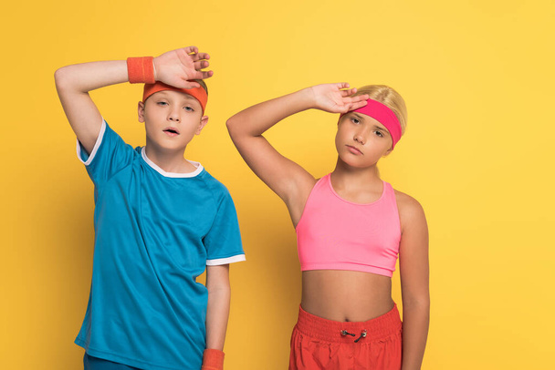 tired kids in sportswear touching heads on yellow background  - Φωτογραφία, εικόνα