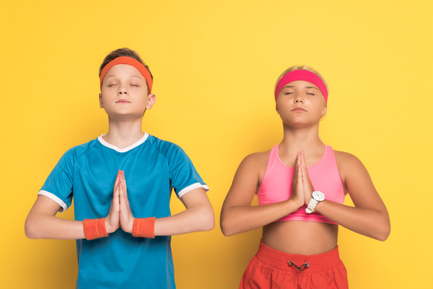 Spor giyinmiş, gözleri kapalı, sarı arka planda dua eden ellerini gösteren çocuklar.  - Fotoğraf, Görsel