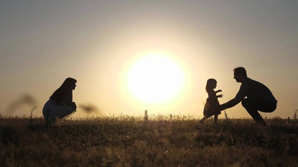 parents play with their little daughter. happy baby goes from dad to mom. happy childhood concept. parents are taught to walk a small child. little girl makes her first steps in sun, slow motion. - Photo, Image