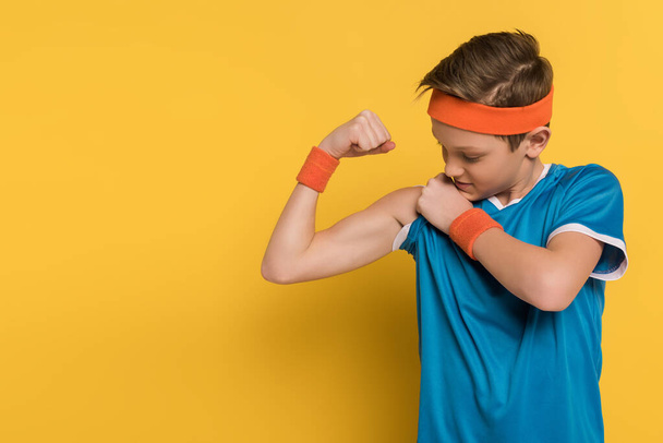dítě ve sportovním oblečení ukazuje svaly na žlutém pozadí  - Fotografie, Obrázek