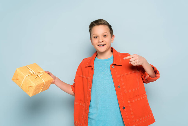 niño sonriente apuntando con el dedo a la caja de regalo sobre fondo azul
  - Foto, Imagen