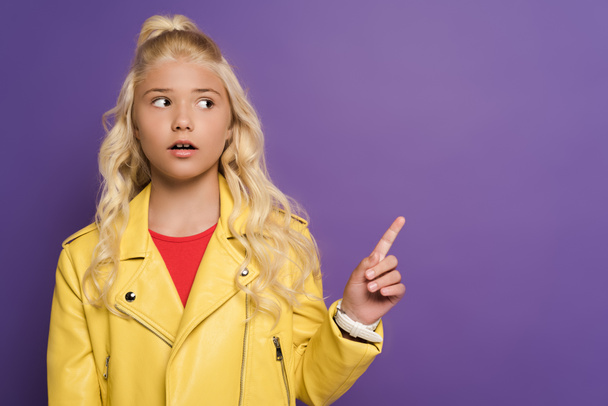 shocked and cute kid pointing with finger on purple background  - Фото, изображение