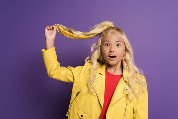 shocked and cute kid touching hair on purple background  - Foto, immagini