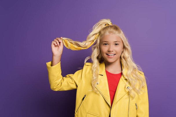 smiling and cute kid touching hair on purple background  - Photo, Image