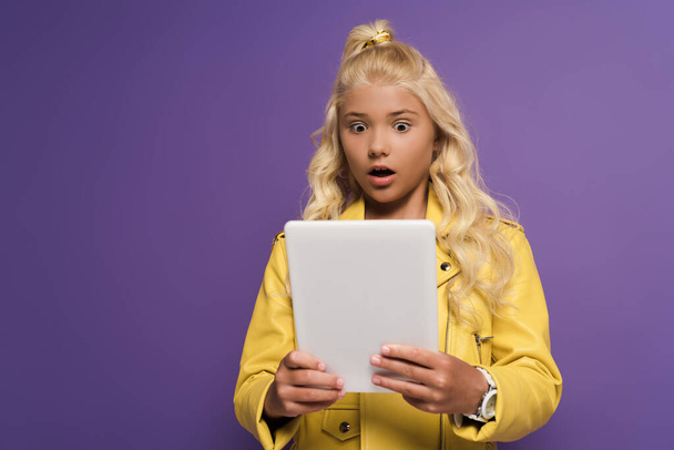 Schockiertes und nettes Kind mit digitalem Tablet auf lila Hintergrund  - Foto, Bild