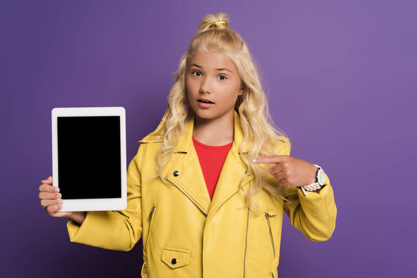 shocked kid pointing with finger at digital tablet with copy space on purple background  - Foto, immagini