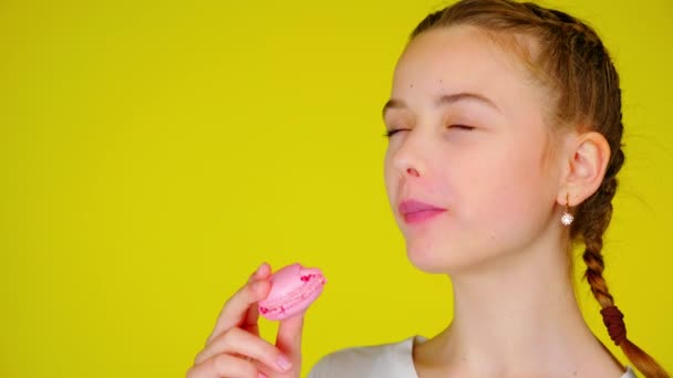 Tiener meisje in een wit T-shirt bijt een roze macaroon en geniet van zijn smaak - Video