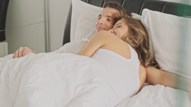 Uma visão de espreitar de um jovem casal apaixonado está deitado em uma cama branca na manhã ensolarada
 - Filmagem, Vídeo