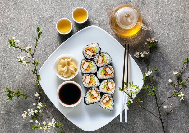 vegan sushi with tofu in General Tso sauce, avocado and fresh vegetables . on a table with branches of a blossoming tree and green tea in a glass teapot - Фото, зображення