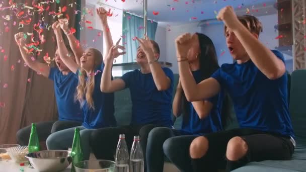 Emotie. Multi-etnische fans vieren het winnen. Confetti 4k slow motion. Gepassioneerde supporters schreeuwen kijken naar wedstrijd op TV. - Video