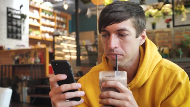 Mies käyttää älypuhelimen kosketusnäyttöä nykyaikaisessa kahvilassa. Mies Juominen pirtelö tai smoothie ja tekstiviestejä älypuhelimella kahvilassa
 - Materiaali, video
