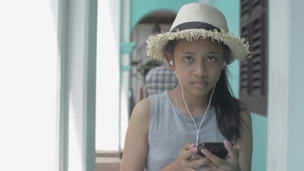 Tayland, Phuket 'te Çin tarzı bir binada, atari salonunda cep telefonu ve kulaklık takan sıradan giysili Asyalı tatlı bir kız. Yavaş çekim. - Video, Çekim