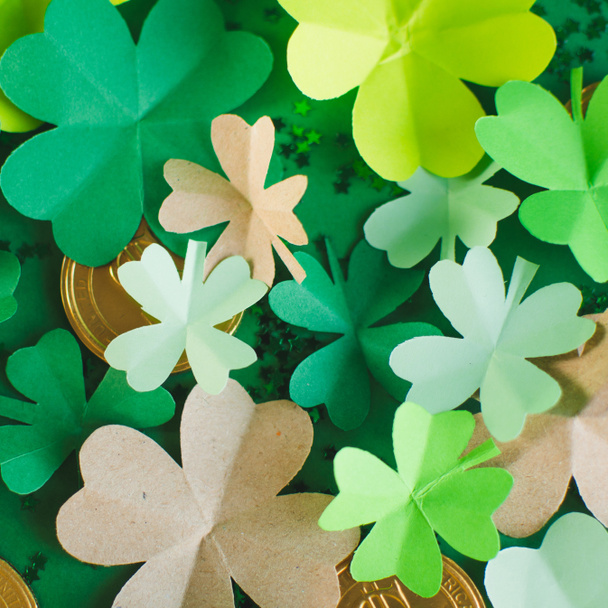 Top view of different shades of green four-leafed paper shamrocks with chocolate coins arranged in chaotic order. Saint Patricks day and lucky concept. Square form - Photo, Image